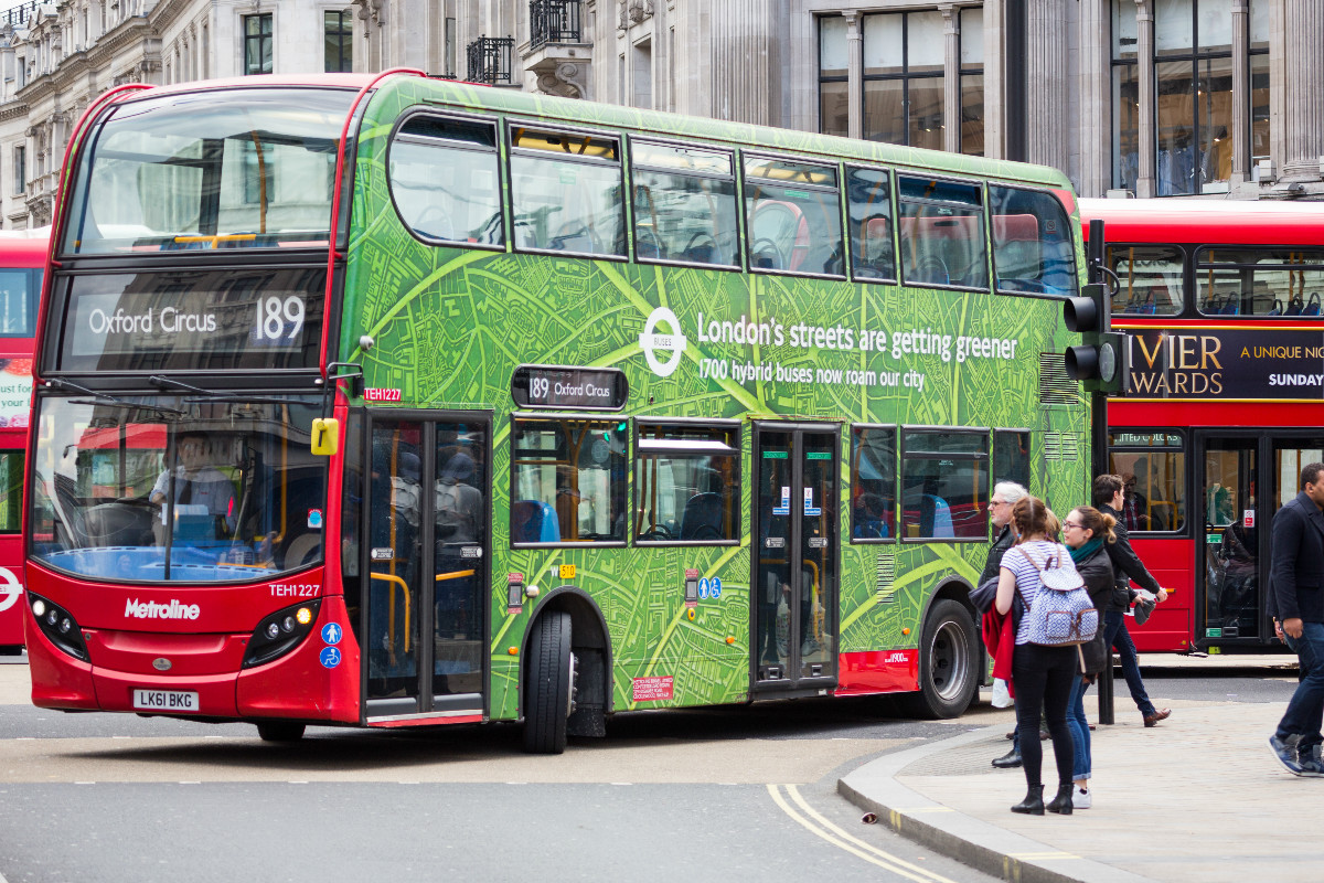 London Bus with green hybrid buses promotion turning Oxford Circus