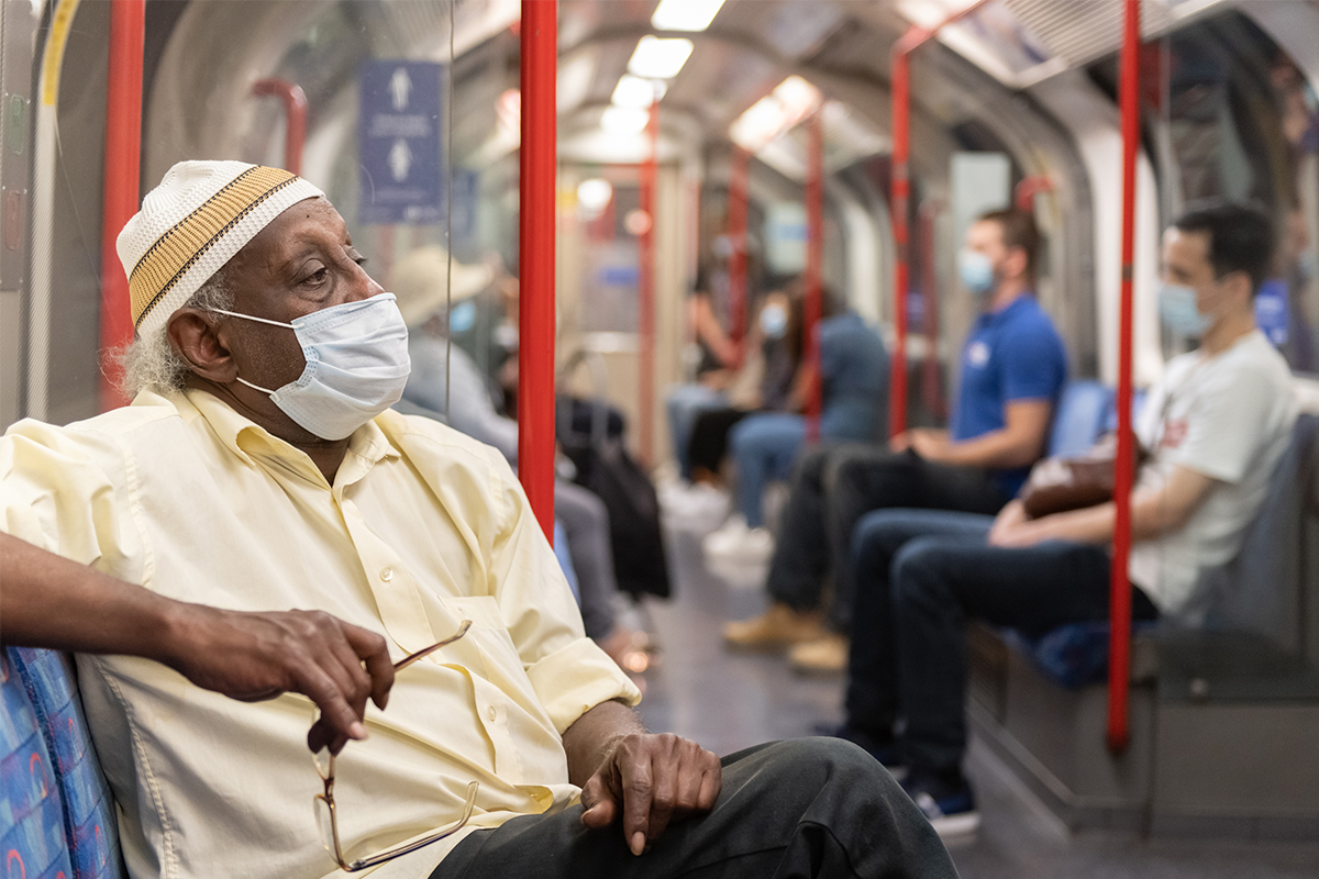 Man sitting on a Tube carriage wearing a face covering
